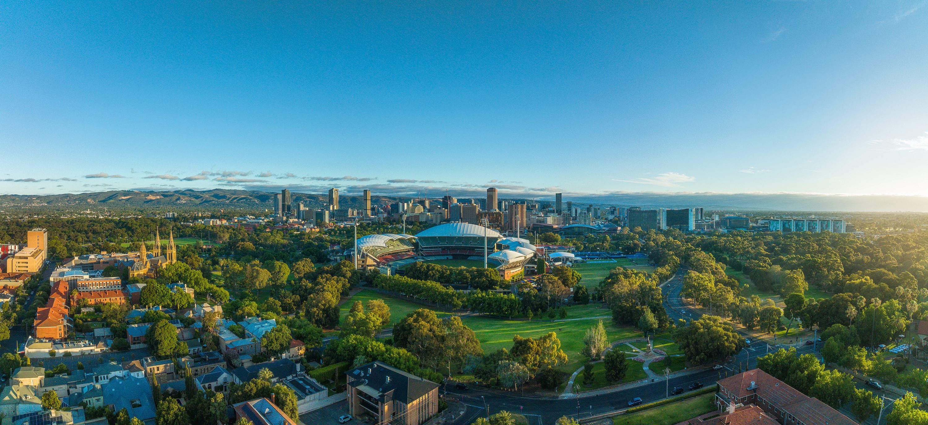 Green aerial photograph of Adelaide's skyline including Adelaide Oval, buildings, churches and parklands